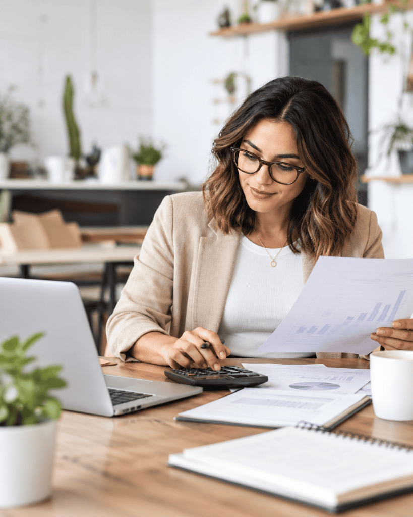 Woman analyzing data with laptop and calculator in an office.