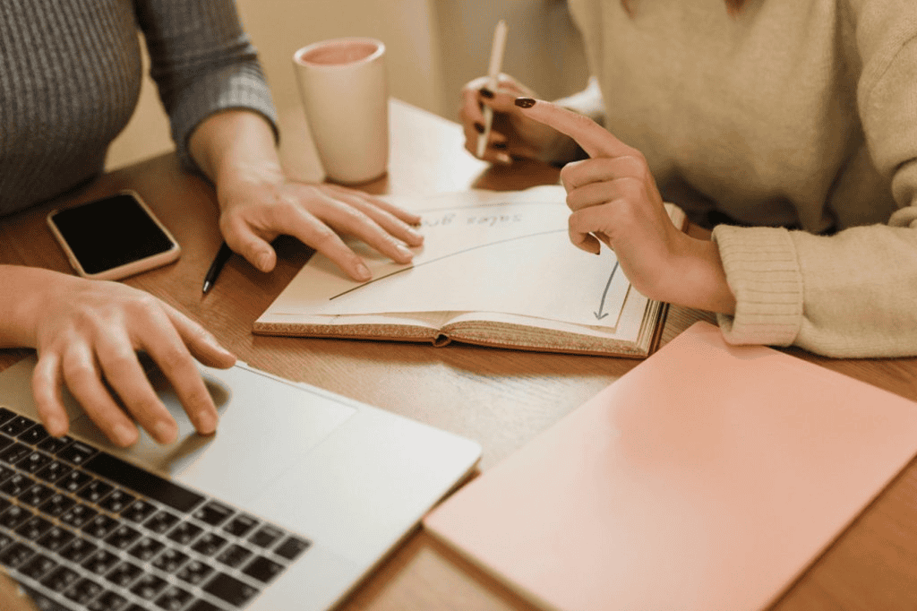 Two people discussing over a notebook and laptop.